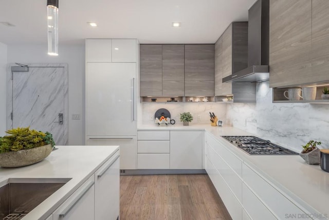 kitchen with tasteful backsplash, light hardwood / wood-style flooring, hanging light fixtures, white cabinets, and wall chimney exhaust hood