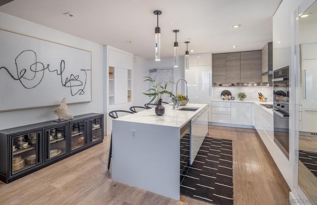 kitchen with decorative light fixtures, sink, light hardwood / wood-style flooring, an island with sink, and white cabinets