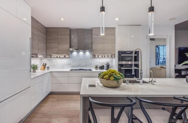 kitchen with wall chimney exhaust hood, a kitchen bar, black appliances, and decorative light fixtures