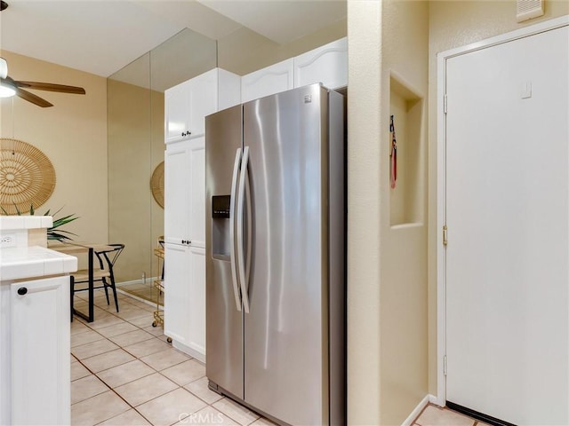 kitchen featuring light tile patterned floors, stainless steel fridge, ceiling fan, white cabinetry, and tile countertops