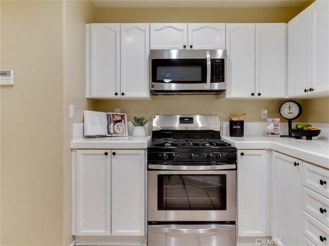 kitchen with appliances with stainless steel finishes, tile counters, and white cabinets