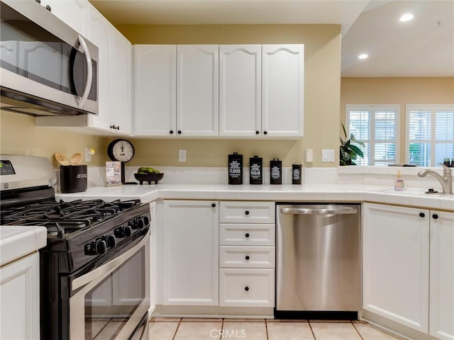 kitchen featuring sink, tile countertops, light tile patterned floors, stainless steel appliances, and white cabinets