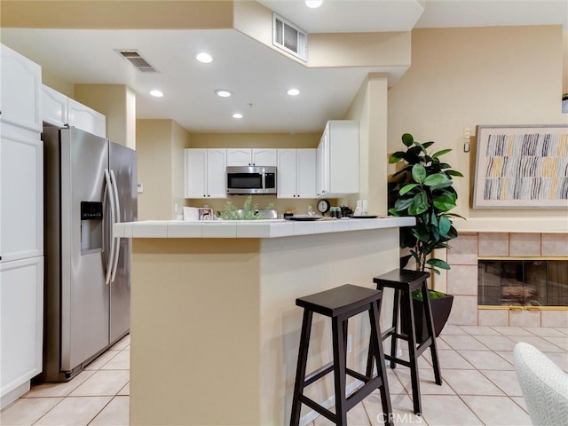 kitchen with white cabinetry, appliances with stainless steel finishes, tile countertops, and a kitchen breakfast bar