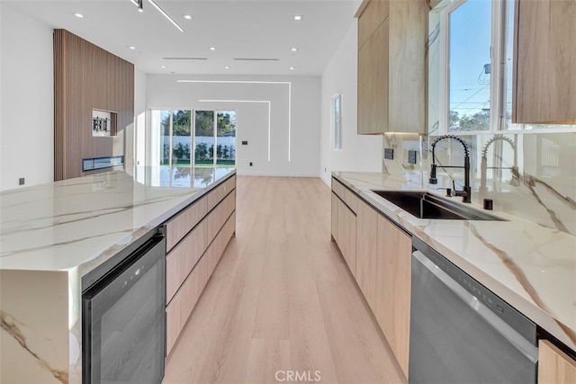 kitchen featuring dishwashing machine, sink, dishwasher, light stone countertops, and light hardwood / wood-style floors