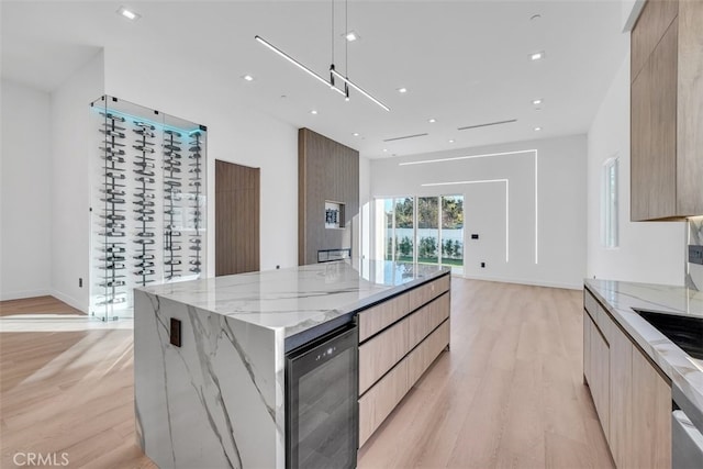 kitchen featuring a large island, light brown cabinetry, light stone counters, and light wood-type flooring