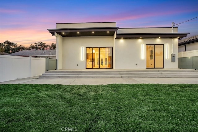 back house at dusk with a lawn and a patio