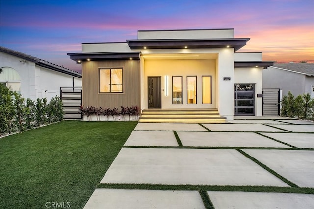 back house at dusk featuring a lawn