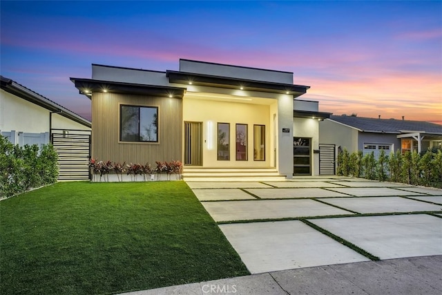 back house at dusk with a patio area and a lawn