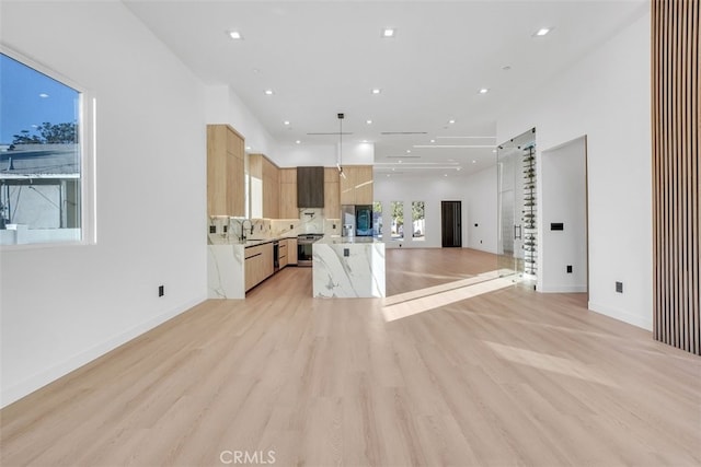 kitchen featuring light brown cabinetry, sink, light stone counters, light wood-type flooring, and pendant lighting