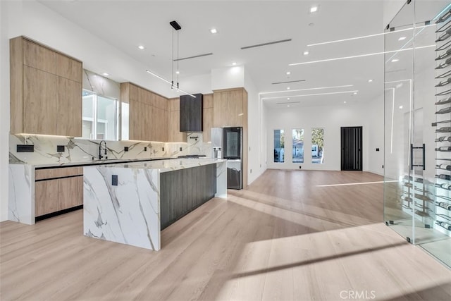 kitchen with tasteful backsplash, light stone countertops, light hardwood / wood-style flooring, and a spacious island