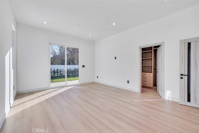 unfurnished bedroom with access to exterior, a spacious closet, and light hardwood / wood-style floors