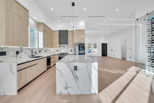 kitchen featuring sink, a spacious island, light stone countertops, stainless steel range with gas cooktop, and light brown cabinets