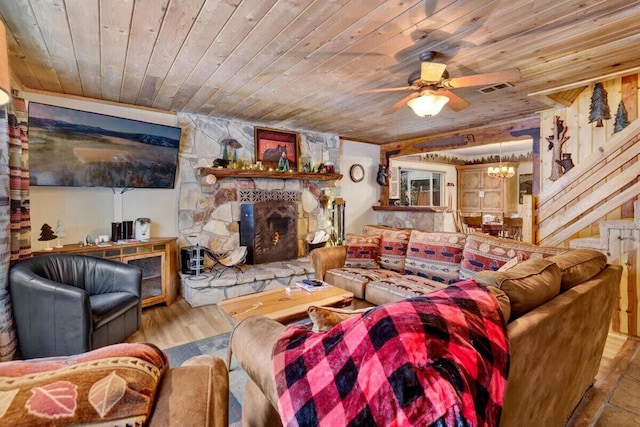 living room with ceiling fan with notable chandelier, light hardwood / wood-style floors, a stone fireplace, and wooden ceiling