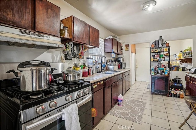 kitchen featuring stainless steel gas range oven, dark brown cabinetry, light tile patterned floors, and sink