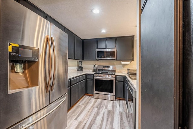 kitchen with light stone countertops, appliances with stainless steel finishes, light wood-type flooring, and a textured ceiling