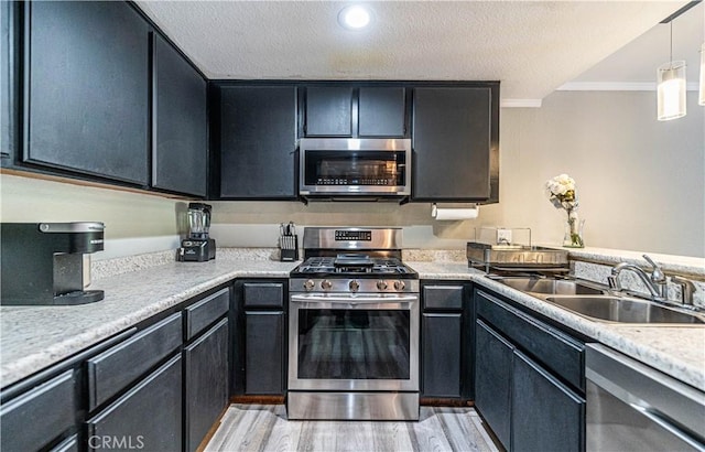 kitchen featuring pendant lighting, sink, crown molding, light wood-type flooring, and appliances with stainless steel finishes