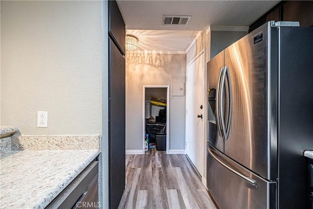 kitchen with light stone counters, stainless steel refrigerator with ice dispenser, crown molding, a textured ceiling, and light wood-type flooring