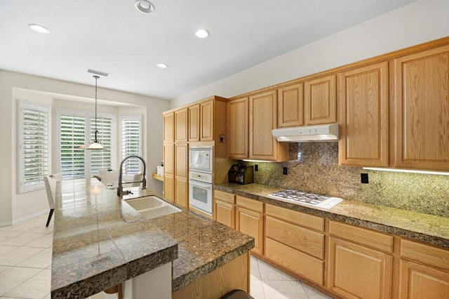 kitchen featuring white appliances, sink, light tile patterned floors, an island with sink, and tasteful backsplash