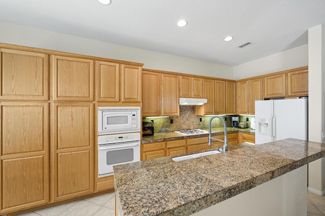 kitchen with backsplash, white appliances, a kitchen island with sink, sink, and light tile patterned flooring