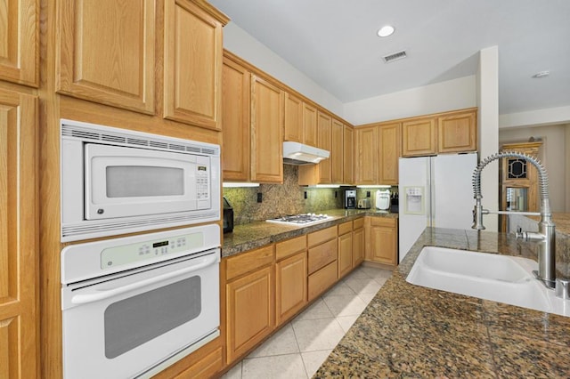 kitchen featuring light tile patterned floors, white appliances, dark stone countertops, and sink