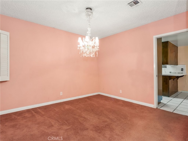 carpeted empty room featuring a textured ceiling and an inviting chandelier