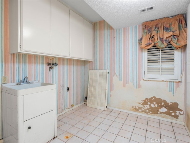 laundry area featuring cabinets, light tile patterned floors, and a textured ceiling