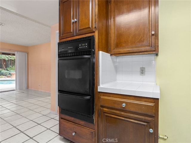 kitchen with backsplash, a textured ceiling, tile countertops, black oven, and light tile patterned flooring