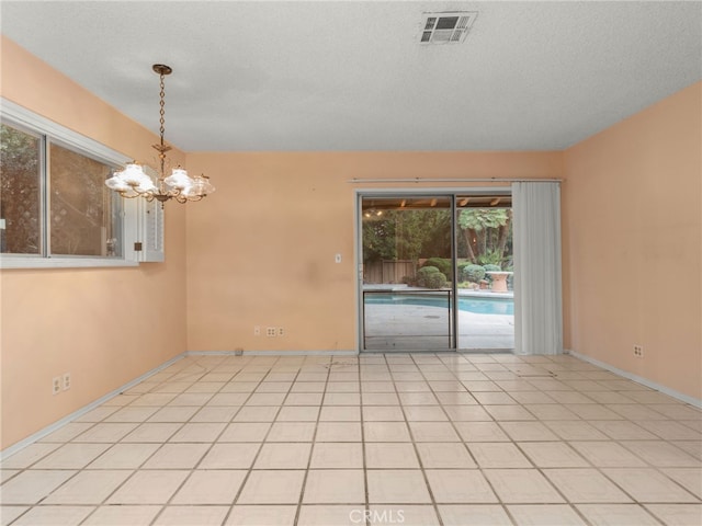 empty room featuring a textured ceiling, an inviting chandelier, and light tile patterned flooring