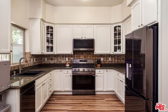 kitchen with sink, light hardwood / wood-style flooring, dark stone counters, white cabinets, and black appliances