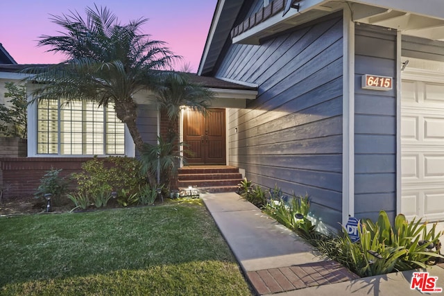 exterior entry at dusk with a lawn and a garage