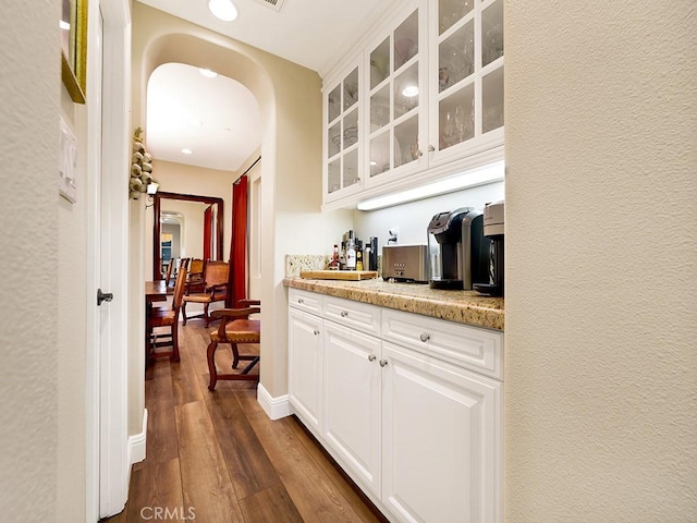 bar with white cabinetry, light stone counters, and dark hardwood / wood-style floors