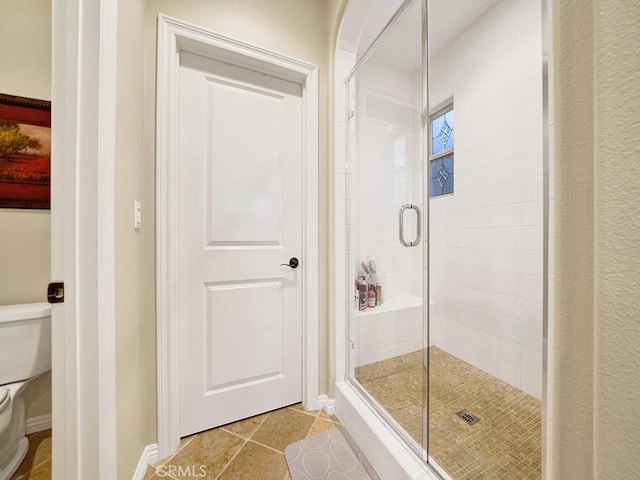 bathroom featuring a shower with door, tile patterned floors, and toilet