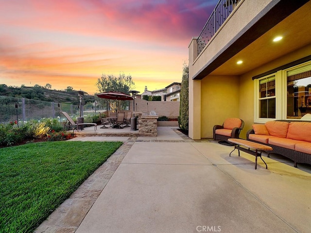 patio terrace at dusk with a balcony, a yard, and an outdoor hangout area