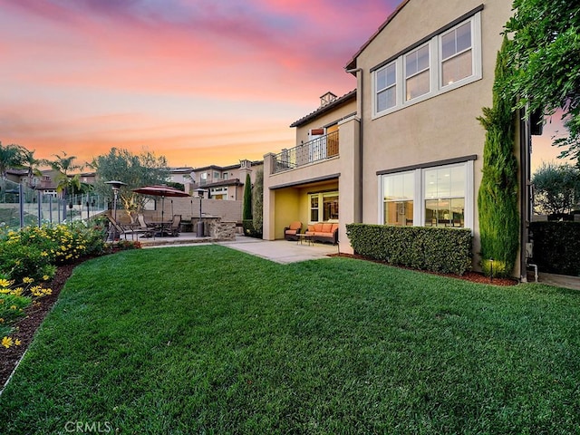 back house at dusk featuring a yard and a patio