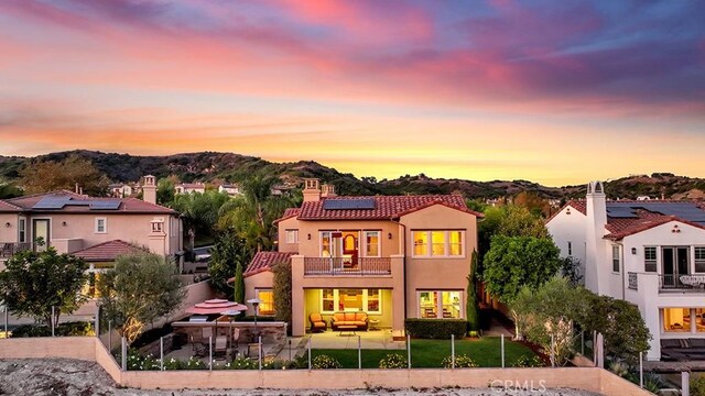 back house at dusk featuring solar panels, a balcony, outdoor lounge area, a patio area, and a mountain view