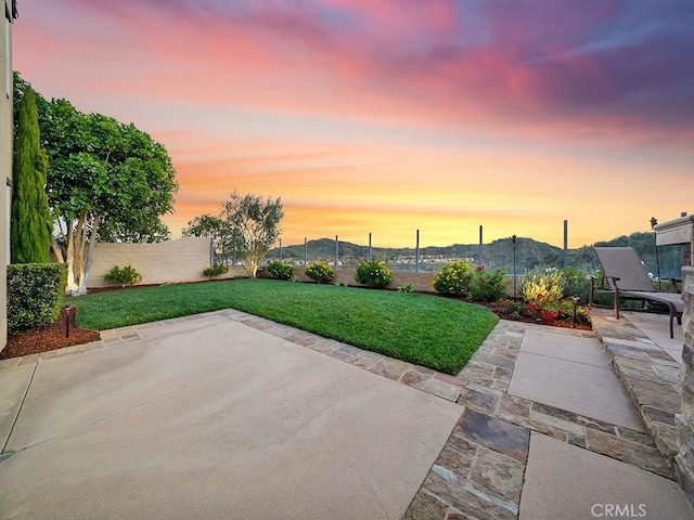 patio terrace at dusk featuring a mountain view and a lawn