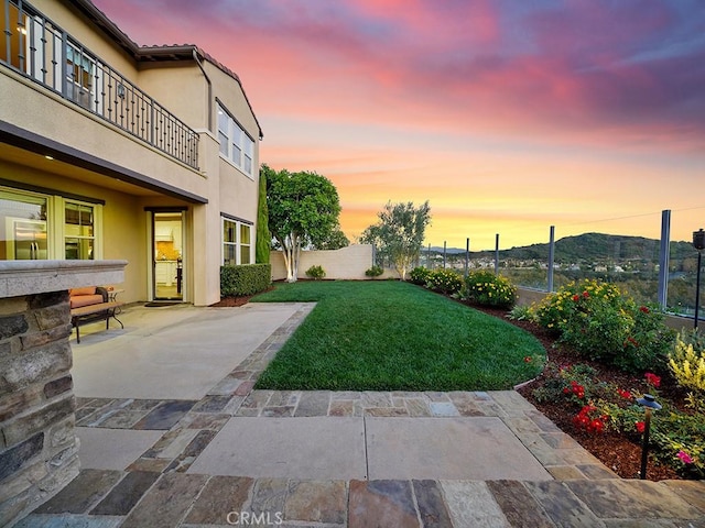 yard at dusk featuring a mountain view, a patio, and a balcony