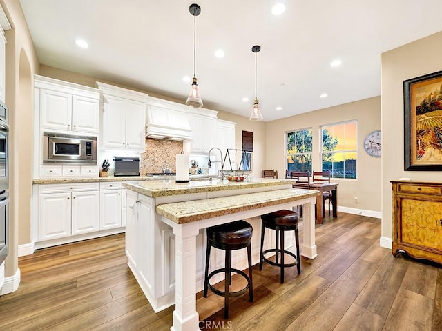 kitchen featuring white cabinetry, pendant lighting, a kitchen island with sink, and wood-type flooring