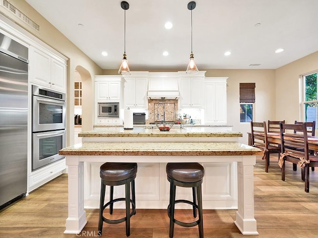 kitchen with white cabinetry, built in appliances, an island with sink, and pendant lighting