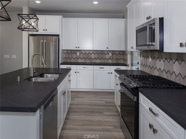 kitchen featuring sink, backsplash, decorative light fixtures, appliances with stainless steel finishes, and light wood-type flooring