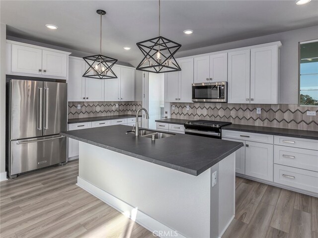 kitchen with appliances with stainless steel finishes, sink, a center island with sink, white cabinetry, and hanging light fixtures