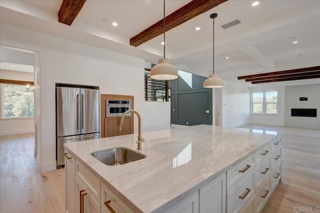 kitchen with sink, decorative light fixtures, light stone counters, and stainless steel appliances