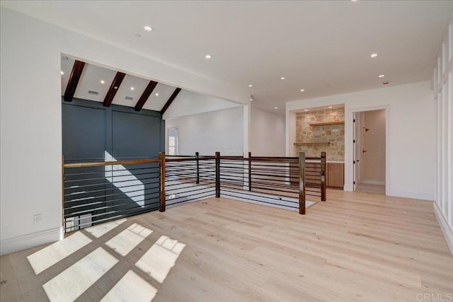 spare room featuring vaulted ceiling with beams, a stone fireplace, and light hardwood / wood-style flooring