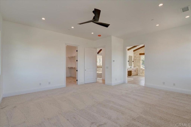 unfurnished bedroom with connected bathroom, ceiling fan, light colored carpet, a walk in closet, and a closet