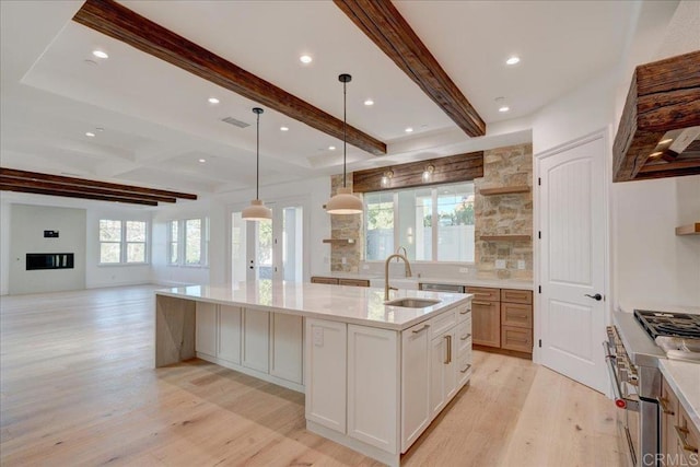 kitchen with sink, backsplash, an island with sink, light hardwood / wood-style floors, and white cabinets