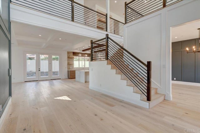 unfurnished living room featuring french doors, light wood-type flooring, a towering ceiling, beamed ceiling, and a chandelier