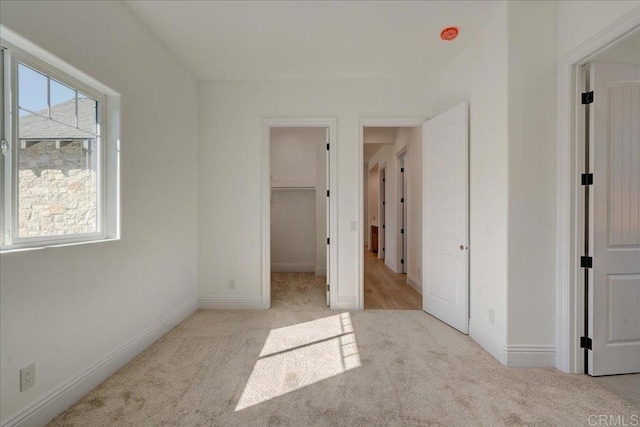 unfurnished bedroom featuring a walk in closet, light carpet, and a closet