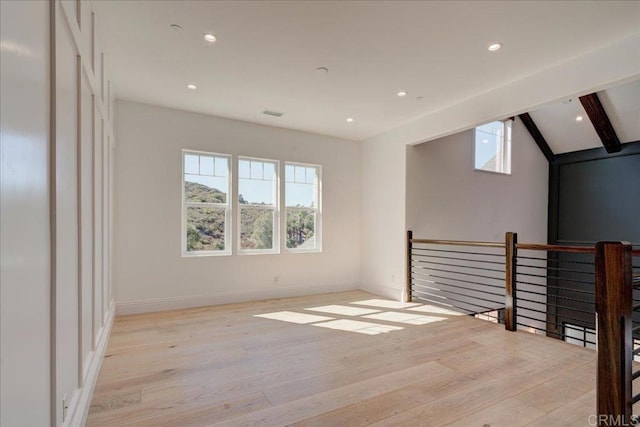 empty room featuring lofted ceiling with beams and light hardwood / wood-style floors