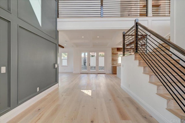 foyer featuring french doors, a towering ceiling, coffered ceiling, beam ceiling, and light hardwood / wood-style flooring