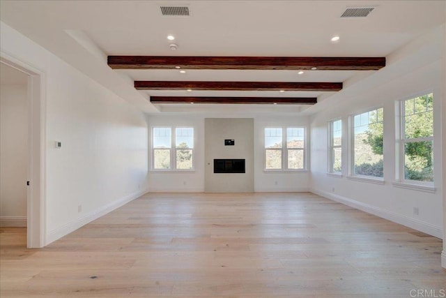 unfurnished living room featuring beam ceiling, a wealth of natural light, and light hardwood / wood-style flooring